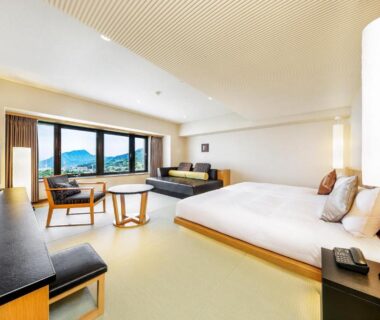 Spacious room with low platform bed, seating area and large window overlooking distant hills at Resorpia Beppu