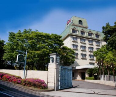 Multi-story hotel entrance with gate, driveway and trees at Resorpia Beppu in Ōita, Kyūshū