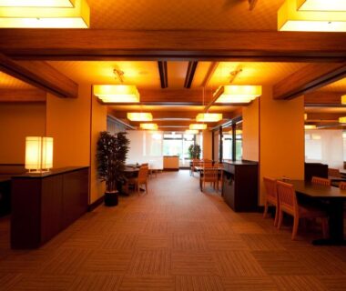 Spacious lounge corridor with seating, wooden beams and warm lantern lighting at Resorpia Beppu, Ōita