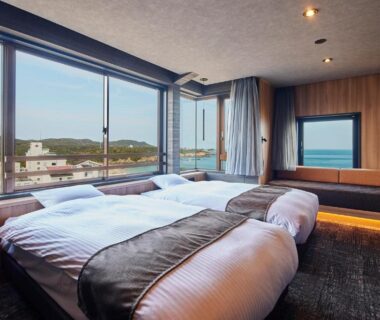 Twin beds with floor-to-ceiling windows and distant sea view at Resort Hills Toyohama Soranokaze in Mie, Kansai