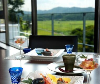 Dining table with plated dishes and glassware overlooking green fields and distant hills at Resort Hills Toyohama Soranokaze, Mie