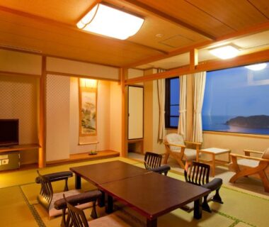 Tatami room with low table, floor chairs and large window overlooking coastal waters at Resort Hills Toyohama Soranokaze in Mie