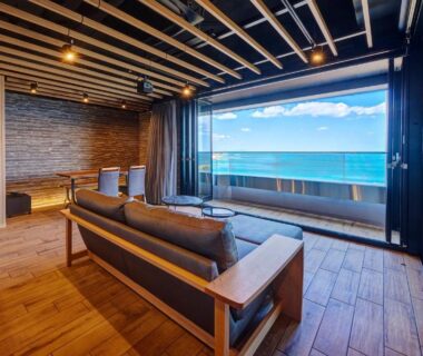 Modern wooden interior with sofa and floor-to-ceiling window overlooking sea at Resort Hills Toyohama in Mie