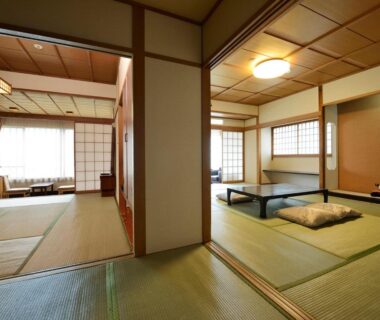 Spacious connected tatami rooms with low table, cushions, shoji screens and natural light at Riverside Uedakan in Nagano