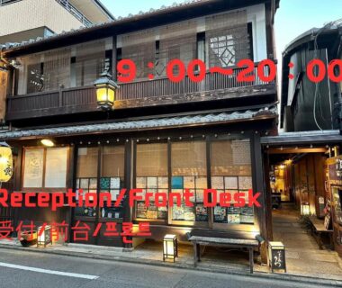 Traditional wooden facade with paper lanterns, bench, entrance and reception hours signage at Roman Kan, Kyoto