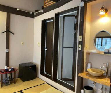 Tatami-floored room with low table, tea set, wooden beams and a small sink area at Roman Kan Kyoto