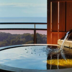 Wooden soaking tub on balcony overlooking sea and coastal treeline at Rurika ryokan Shizuoka