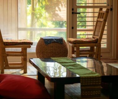 Tatami room with low table, cushions, wooden chairs and sliding doors opening to leafy garden at Rurika in Shizuoka