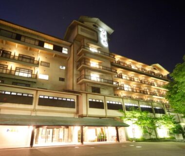 Illuminated multi-story façade of Rurikoh ryokan at night with balconies and lit entrance in Ishikawa, Chūbu, Japan