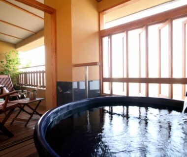 Round onsen tub with flowing water, wooden deck seating and shoji-style windows at Rurikoh in Ishikawa