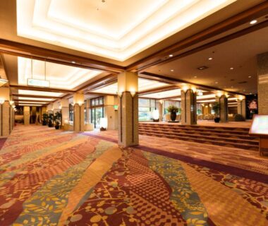 Carpeted lobby corridor with columns, warm ceiling lighting and seating at Rurikoh in Ishikawa, Chūbu