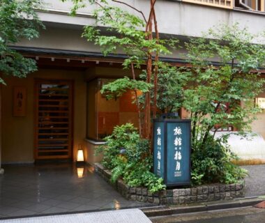 Entrance of Ryokan Asakusa Shigetsu with wooden doorway, illuminated sign and potted greenery in Tokyo