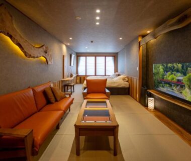 Tatami-floor room with sofa, low wooden table, futon bed, shoji screens and wall-mounted TV in warm lighting