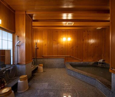 Indoor wooden onsen with washing stations, stools, buckets and stone floor at Ryokan Asunaro in Gifu