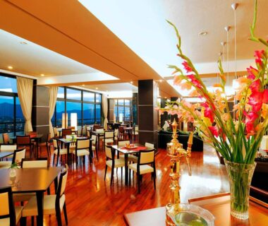 Spacious dining area at Ryokan Biyunoyado with wooden floors, tables and windows framing Nagano mountain views.