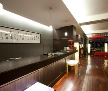 Spacious wooden-floored lobby with dark reception counter, framed calligraphy, seating area and decorative red umbrella