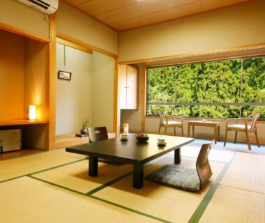 Traditional tatami room with low table, zabuton cushions and large window overlooking wooded greenery in Kyoto ryokan