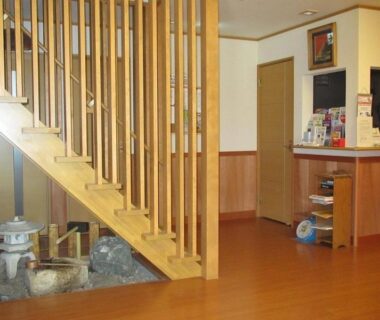 Ryokan entrance hall with wooden staircase, stone accent under stairs and reception counter with brochures in Tokyo
