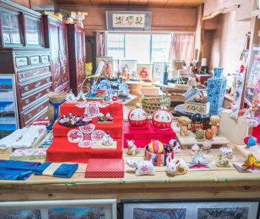 Assorted dolls and ceramics on red cloth in ryokan gift area with wooden interior, Yamanashi