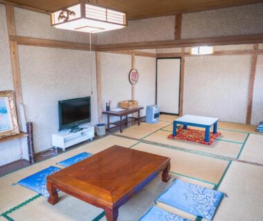 Spacious tatami room with low wooden table, floor cushions and television at Ryokan Fuji Heights in Yamanashi