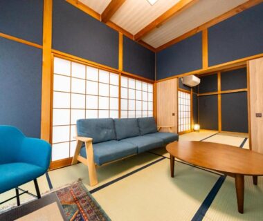Tatami room lounge with shoji screens, blue sofa, round wooden table and tatami mat flooring at Ryokan Fukinoya in Ōita