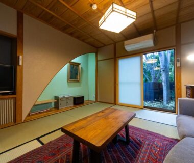 Tatami room with low wooden table, shoji screens, sofa and garden view at Ryokan Fukinoya Ōita
