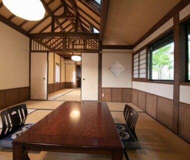 Tatami room with low wooden table and zaisu chairs, shoji windows framing lush greenery at Ryokan Fukinoya, Ōita