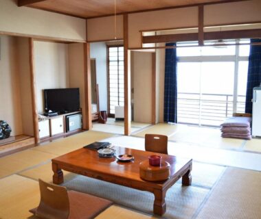 Traditional tatami room with low wooden table, floor chairs, shoji screens and sliding balcony doors at Ryokan Fukuzen, Gunma