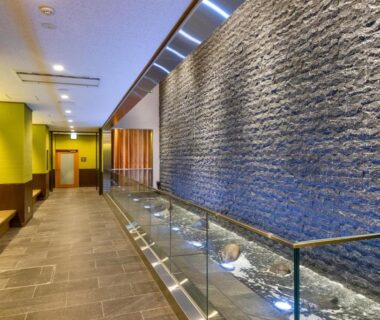 Indoor corridor with textured stone water wall, glass railing and stone floor at Ryokan Ginkaku Kyoto, Kyoto