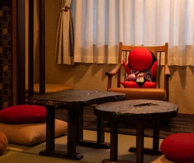 Tatami room with low wooden tables, floor cushions, and a red armchair holding a decorative doll