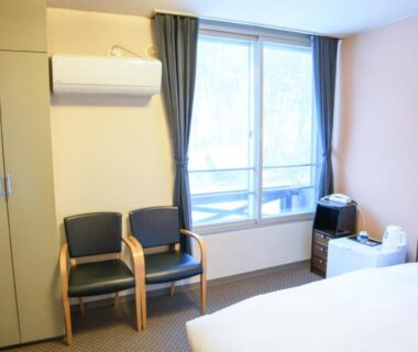 Compact room with bed, chairs, air conditioner and window at Ryokan HANAEMI in Hokkaidō, Japan