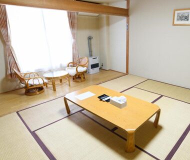 Bright tatami room with low table, wicker chairs and curtained window at Ryokan HANAEMI in Hokkaidō