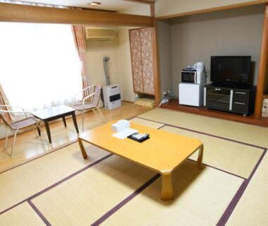Tatami room with low table, TV and window seating at Ryokan HANAEMI in Hokkaidō, Japan