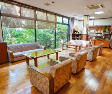 Wooden lounge with armchairs, low tables and large garden-facing windows at Ryokan Hirayama in Kumamoto, Kyushu