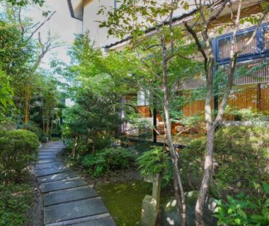 Stone pathway winding through lush traditional ryokan garden beside wooden guest rooms at Ryokan Hirayama in Kumamoto, Kyushu