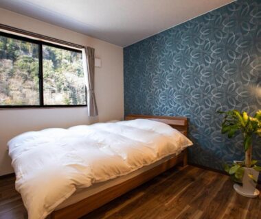 White duvet bedroom with patterned accent wall at Ryokan Hitaya Ōita wooden floors and hillside view