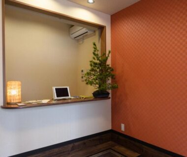 Compact reception counter with lamp, tablet, potted plant and patterned orange wall at Ryokan Ichinao in Tokyo
