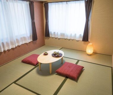 Traditional tatami room with low table, red floor cushions and soft lantern lighting at Ryokan Ichinao in Tokyo