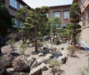Japanese courtyard garden with pruned trees, rock landscaping and sand pathways between ryokan buildings