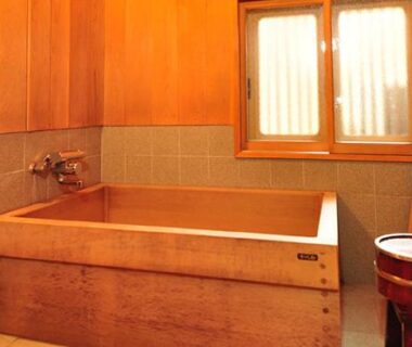 Wooden bathing room with soaking tub, handheld shower, tiled walls and wooden bucket at Ryokan Imai, Niigata