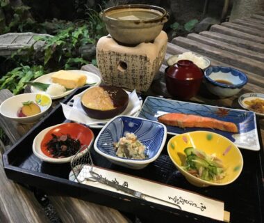 Tray of assorted Japanese dishes including grilled salmon, rice, pickles and soup on a wooden table at Ryokan Inakatei
