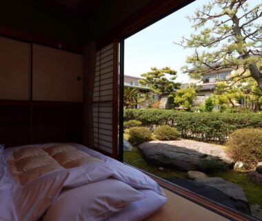 Futon on tatami by open shoji overlooking a manicured garden with stones and pines at Ryokan Karasawa Ishikawa