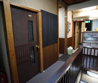 Narrow wooden interior corridor with guest room doors and stair railing at Ryokan Katsutaro in Tokyo