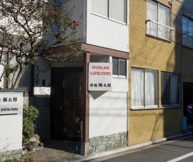 Narrow street-front ryokan entrance with bilingual signage and stone base in Tokyo neighborhood