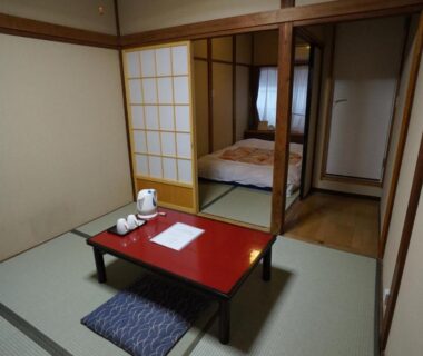 Tatami room with red low table, zabuton cushion and futon visible through shoji at Ryokan Katsutaro Tokyo