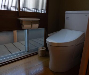 Modern Japanese toilet with wooden floor, shoji-style window and small wooden bucket at Ryokan Kiraku Oita