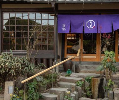 Front entrance with stone steps, wooden facade and purple noren at Ryokan Kiraku in Ōita, Kyūshū