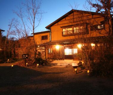 Evening-lit wooden ryokan facade with shoji windows and entrance path