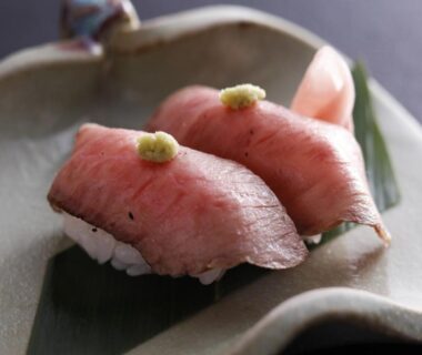 Two seared meat nigiri with green paste garnish on ceramic plate with leaf