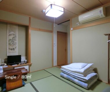 Traditional tatami room with stacked futons, low table, wall scroll and air conditioning at Ryokan Kyoraku in Kyoto